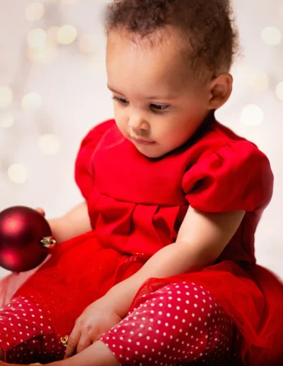 Baby in a red dress holding a Christmas ornament