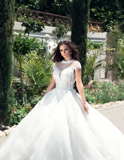 Bride in a full white wedding gown holding a bouquet beside columns
