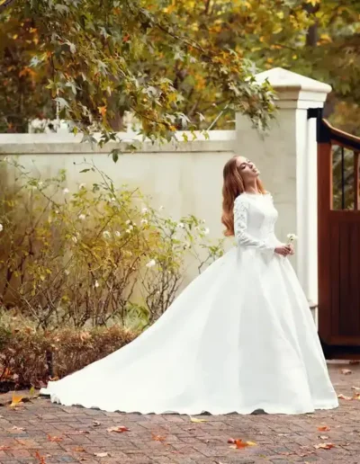 Red-haired bride in a long white wedding gown surrounded by autumn trees