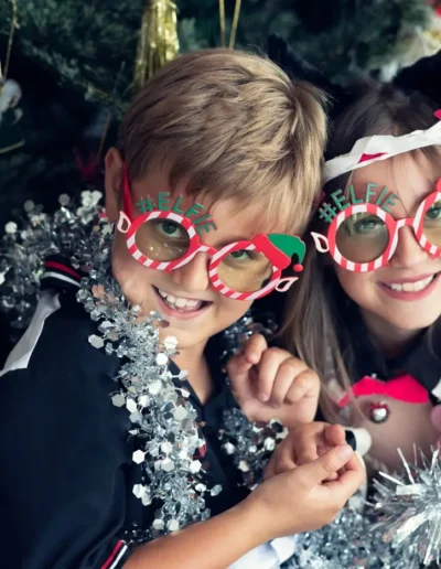 Brother and sister wearing festive glasses during a Christmas portrait