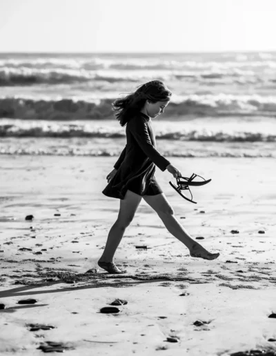 Young girl walking barefoot along the beach in a black and white portrait