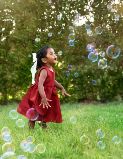 Young girl in a red dress playing with bubbles outdoors