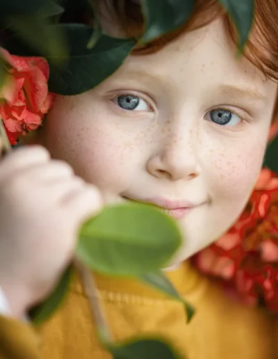 Red-haired boy with freckles surrounded by flowers and green leaves