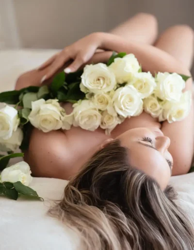 Woman reclining among white roses during a romantic boudoir photoshoot