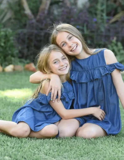 Two sisters in blue dresses sitting together on the grass