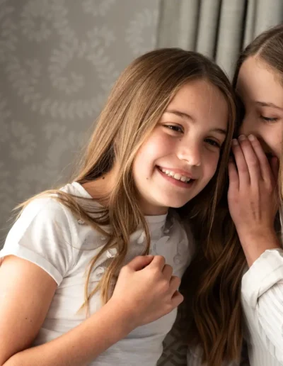 Two sisters smiling and whispering together during an indoor portrait